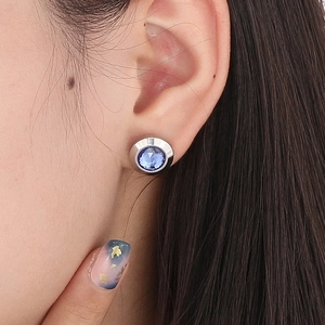 Close-up of elegant silver stud earrings featuring a faceted blue crystal on model ear