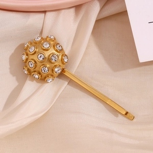 Macro detail of golden metal hair clip featuring a spherical rhinestone stud on silk background