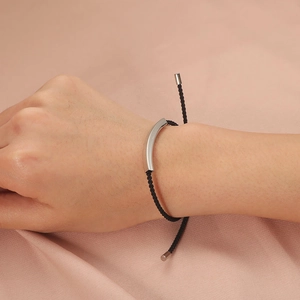 Minimalist stainless steel hollow tube bracelet with black woven cord on satin background