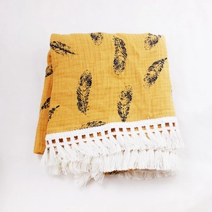 Close-up of yellow cotton baby blanket with black feather print and white tassel trim