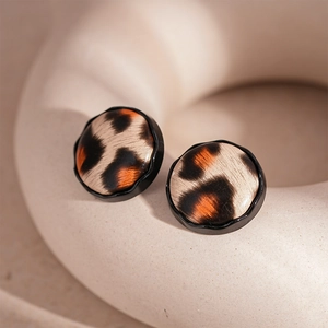 Detailed close-up of round leopard print earrings on a white ceramic display