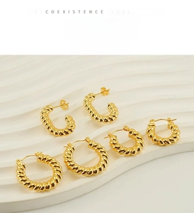 Detailed view of three pairs of vintage gold twisted hoop earrings on a white tray