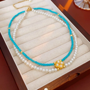 Dettaglio di collana a due strati con perle bianche, grani turchesi e ciondolo a quadrifoglio