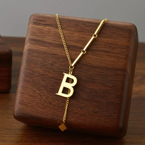 Titanium steel gold necklace with letter B pendant and tassel on a wooden display stand