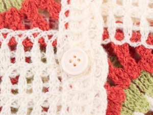 Detail of crochet knit texture with colorful stripes and a white button on cardigan