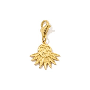 Detail of a gold sun pendant with a hammered round center and radiating rays on a white background