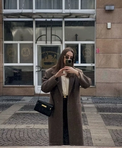 Detail of long brown wool coat with waist belt and black leather shoulder bag