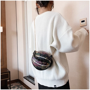 Close-up of a round black graffiti crossbody bag with golden chain on a model back