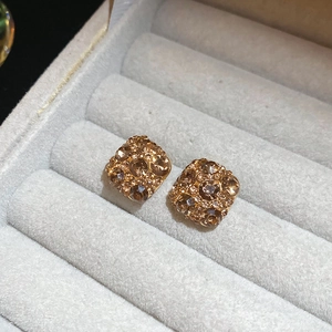 Macro shot of gold-plated square stud earrings with champagne crystals in a grey jewelry box