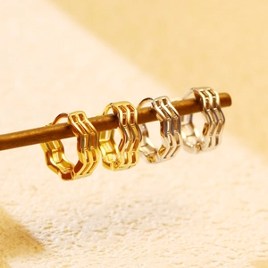 Detailed view of gold and silver S925 sterling silver wavy hoop earrings on a wood branch