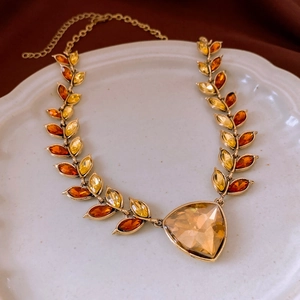 Detail of wheat ear necklace with amber crystals on vintage ceramic plate and brown fabric