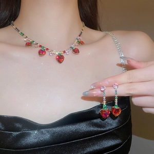 Close-up of luxury gold necklace and earrings set with red heart gems and zircon tassels