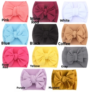 Flat lay of soft knit baby headbands with large bows in 11 different assorted colors