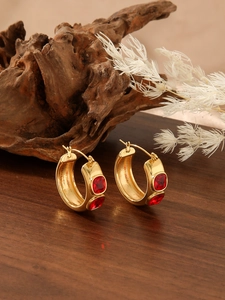 Chic gold hoop earrings with baguette-cut red zircons displayed on a rustic wood surface