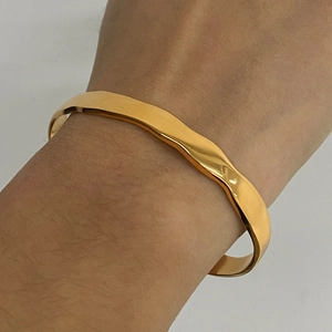 Detail of 18K gold-plated stainless steel open bangle with irregular wavy pattern