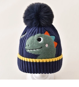 Close-up of navy knit baby hat with green dinosaur pattern and faux fur pompom