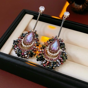 Detailed view of teardrop crystal earrings with pink gemstones on beige jewelry cushion
