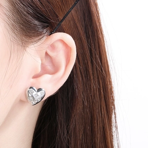 Close-up of sparkling heart-shaped silver stud earrings worn on a model's earlobe