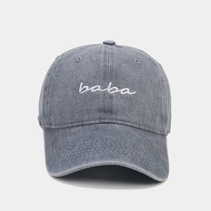 Close-up of white cursive baba embroidery on washed gray-blue denim baseball cap