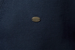 Detail of a bronze metal logo on dark blue knit sweater with fine ribbed texture