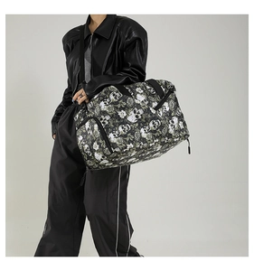 Detailed view of large black travel bag with skull and rose print worn by model