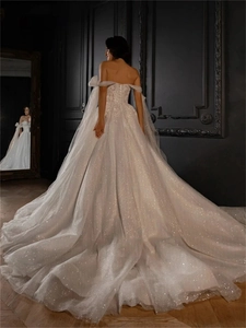 Detail of a white off-shoulder bridal gown featuring shimmering sequined starburst fabric