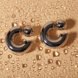 Macro shot of silver C-shaped minimalist earrings with double ball closure and water droplets