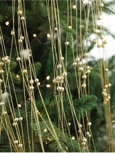 Détail d'une guirlande de perles dorées brillantes sur un sapin de Noël avec lumières bokeh