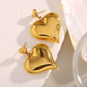 Macro close-up of chunky gold heart stud earrings on a textured stone base