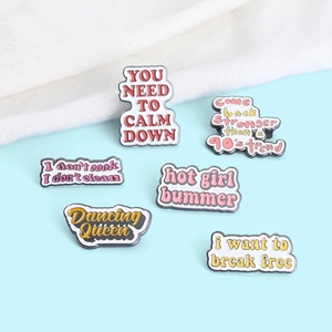 Close-up of six colorful enamel pins with pop culture slogans on blue and white fabric