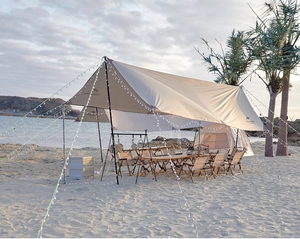 Outdoor beige camping canopy with warm LED string lights set up on a beach at sunset