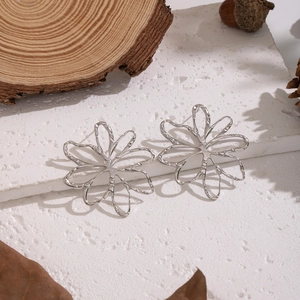 Macro shot of silver hollow line flower earrings on white stone with natural props