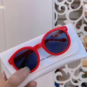 Close-up of red round kids sunglasses with dark lenses and a white leather case