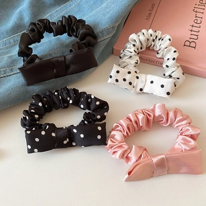 Close-up of four satin bow scrunchies in polka dot and solid colors on denim
