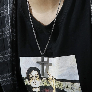 Detail of a dark stainless steel cross pendant on a twist chain necklace worn by a model