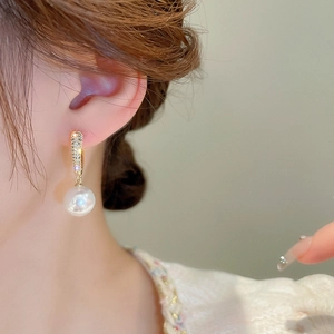 Elegant gold plated heart earrings with zircon and pearls worn by a model in warm light