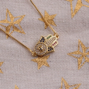 Gold Hamsa hand necklace with colorful zircon stones on a star pattern background