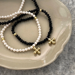 Elegant pearl and black beaded necklaces with gold cross charms on a ceramic tray