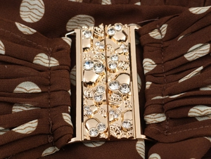 Detail of golden skull buckle with rhinestones on a brown polka dot pleated dress