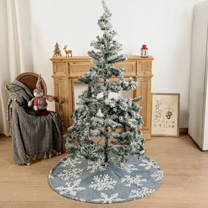 Blue Christmas tree skirt with white snowflake pattern and flocked tree by a fireplace