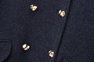 Détail du tissu en laine mélangée bleu foncé avec quatre boutons dorés et texture sergé