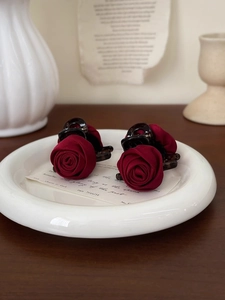 Close-up of two vintage red rose hair claws on a ceramic plate with decorative cards