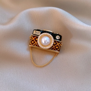 Macro detail of vintage camera brooch with 14k gold plating, pearl lens and enamel inlay
