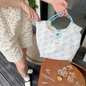 Detail of canvas tote bag featuring floral bear patterns and blue woven rope handles