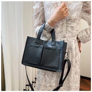 Detail of a vintage black PU leather tote bag with square front pockets and a shoulder strap