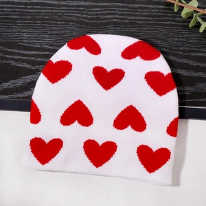 Berretto in maglia bianca con cuori rossi su sfondo in legno scuro e bianco