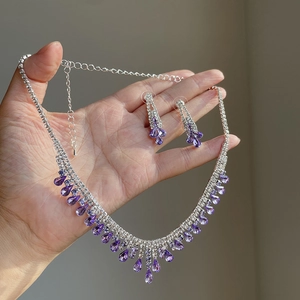 Elegant silver necklace and earring set with purple teardrop rhinestones on hand