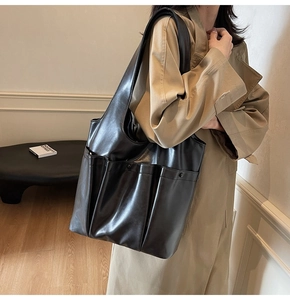 Detail of large black PU leather tote bag with functional pockets on a khaki coat