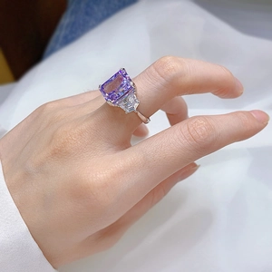 Macro shot of rectangular purple gemstone ring with side baguette stones on hand