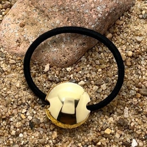 Black elastic hair tie featuring a polished gold metal disc on natural stone background